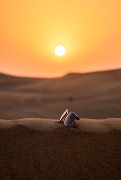 Scenic view of sunglasses on Dubai's desert sand with a stunning sunset backdrop.
